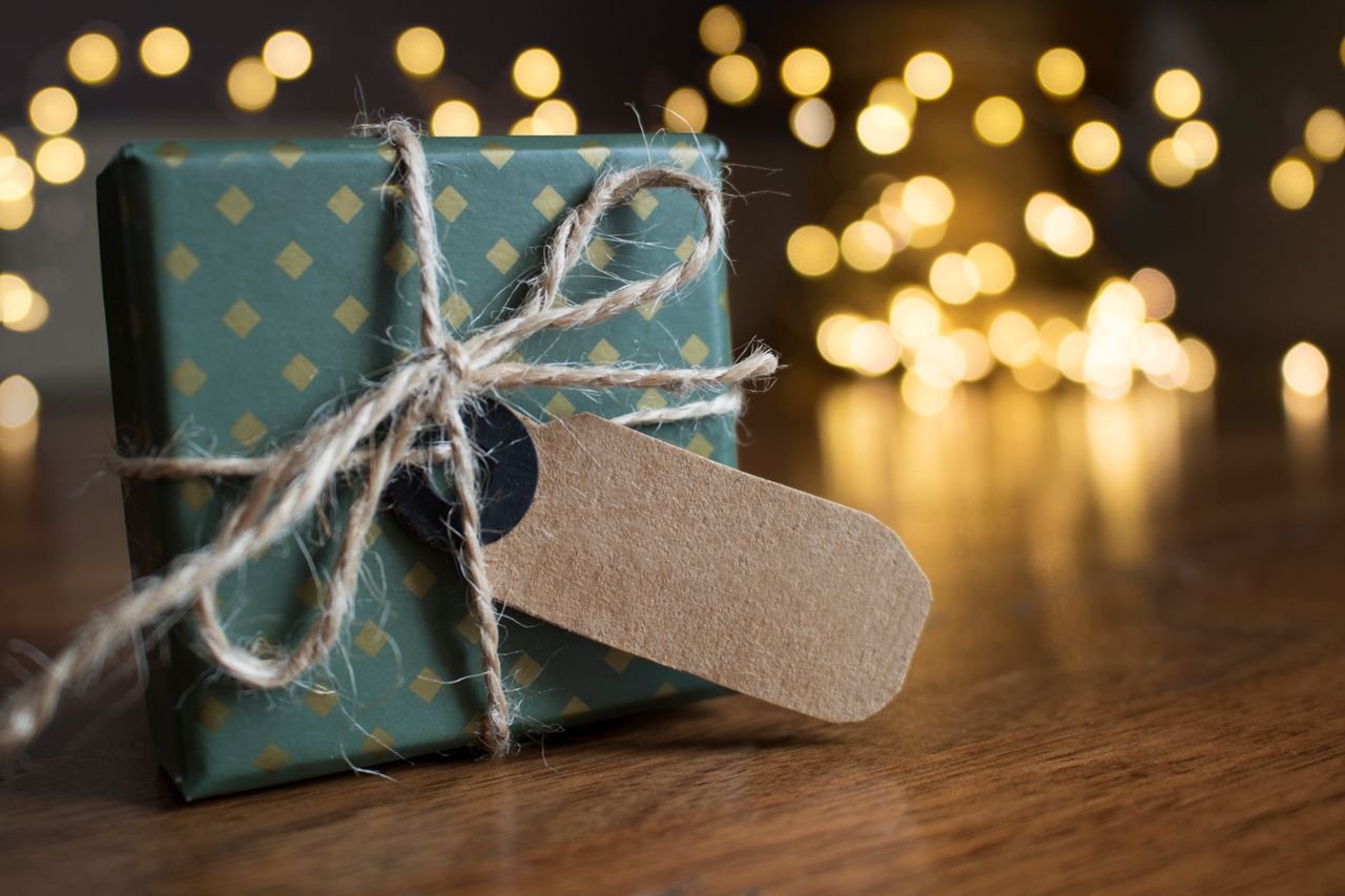A wrapped gift box with twine beside festive bokeh lights indoors.
