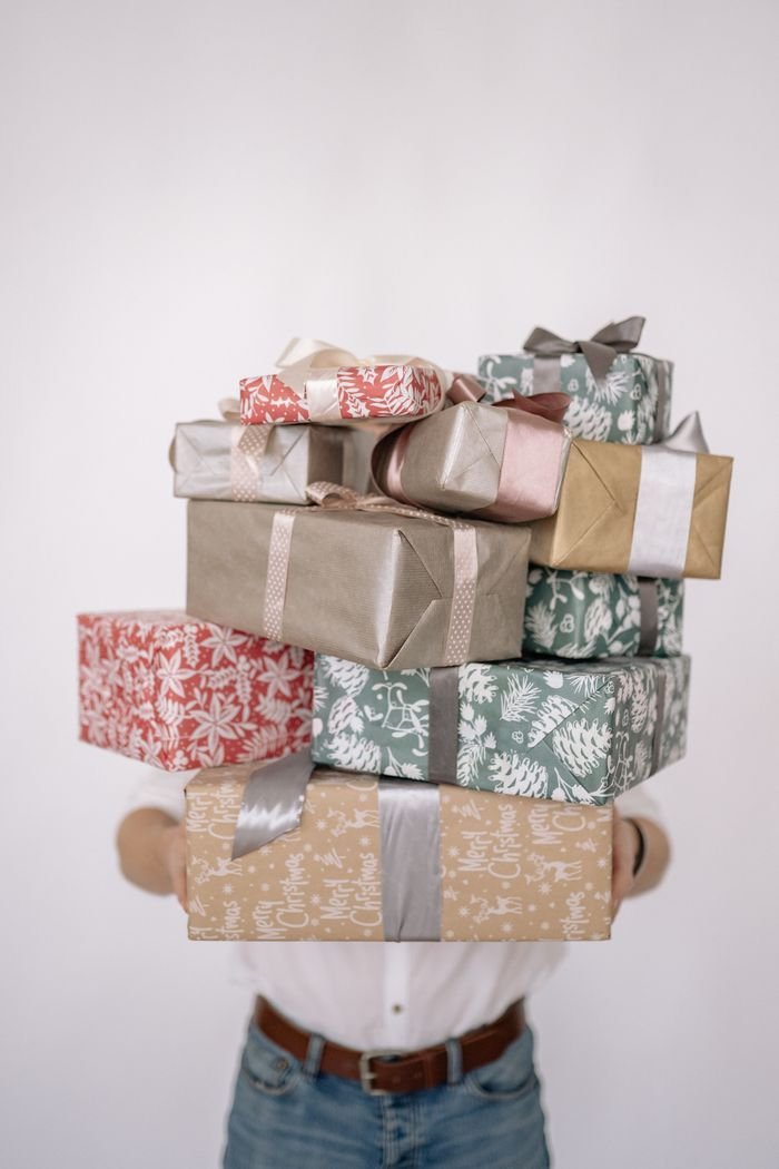 Home Person holding a stack of colorful wrapped gifts against a plain white background.