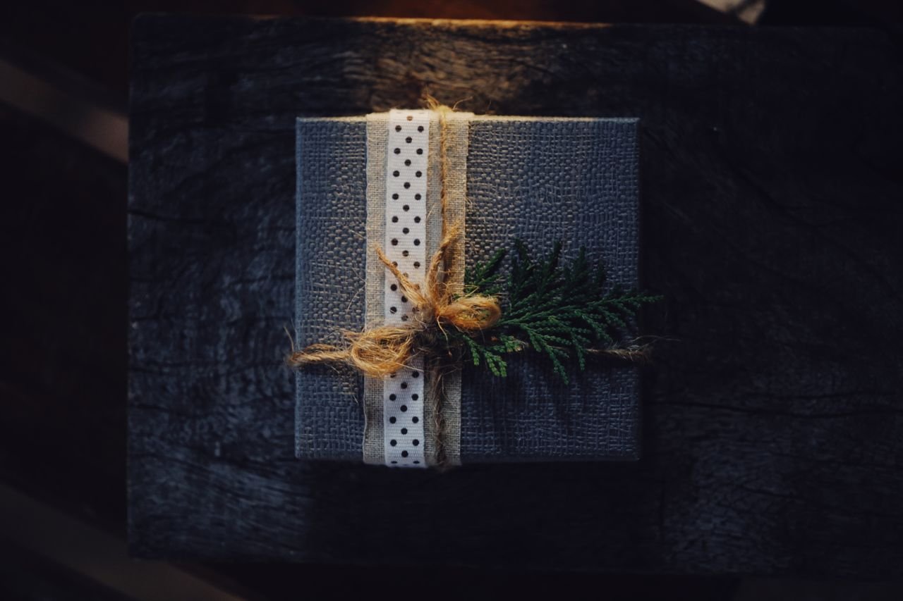 Elegant rustic gift box with polka dot ribbon and fern decoration on a dark wooden background.